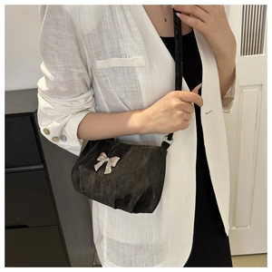 Detail of black pleated shoulder bag with a metallic silver bow buckle on white blazer