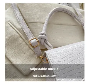 Detail of white crocodile embossed leather bag with gold buckle and knotted handle strap