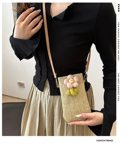 Detailed view of woven straw crossbody phone bag with 3D floral decoration and leather strap