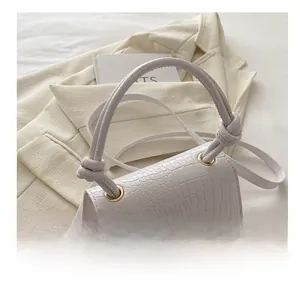 Close-up of white crocodile pattern bag with knotted handle on a beige blazer