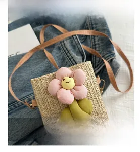 Detail of light beige straw crossbody bag featuring pink sunflower with smiley face