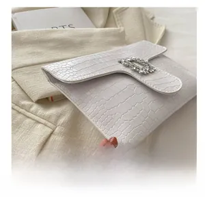 Detail view of white crocodile pattern envelope clutch with sparkling rhinestone buckle