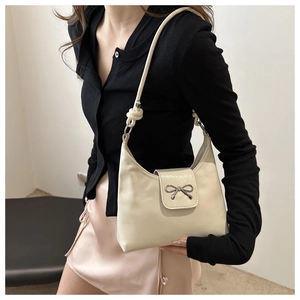 Détail du sac hobo blanc cassé avec une élégante boucle de nœud argentée sur le rabat
