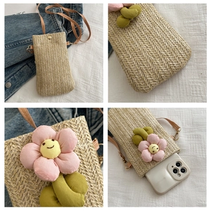 Detail view of woven straw mobile bag featuring a 3D floral smile patch and thin strap