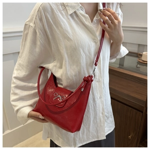 Détail du sac à bandoulière en cuir rouge brillant avec boucle en nœud argenté