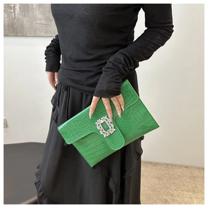 Close-up of green crocodile-textured envelope clutch featuring a brilliant diamond buckle