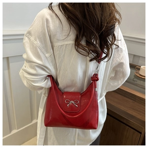 Détail du sac demi-lune rouge avec nœud métallique sur fond de chemise blanche