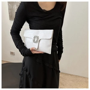 Close-up of a white crocodile embossed envelope clutch bag with a rhinestone buckle