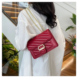 Detail of red quilted chain crossbody bag with golden rectangular clasp on a model