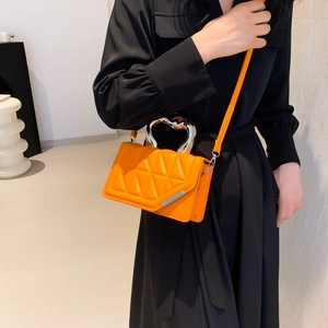 Orange quilted crossbody bag with silver ring handle and metal strap on dark dress