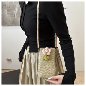 Detail of woven straw phone bag featuring 3D floral accents and elegant metal strap rings