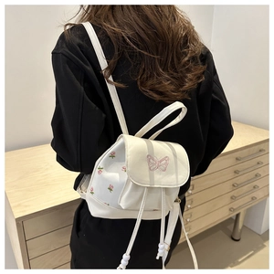 Close-up of white mini backpack featuring delicate pink butterfly and floral embroidery