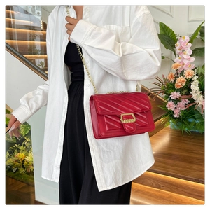 Detail of red quilted leather crossbody bag with V-shaped stitching and gold chain strap