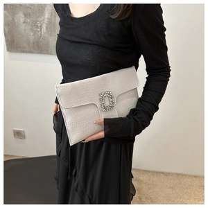 Detail of cream faux leather envelope clutch featuring a crystal buckle and croc texture
