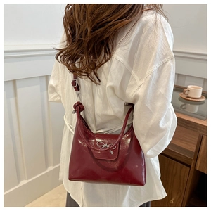 Side view of a wine red PU bucket bag with a silver bow ornament on a female model