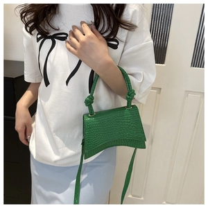Detail view of dark green crocodile pattern bag with curved base and knotted handle