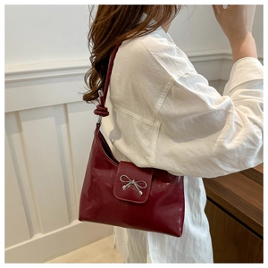 Detail of burgundy glossy leather shoulder bag featuring a decorative silver metal bow