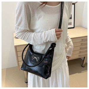 Détail du sac noir brillant avec nœud métallique argenté et fine bandoulière chic