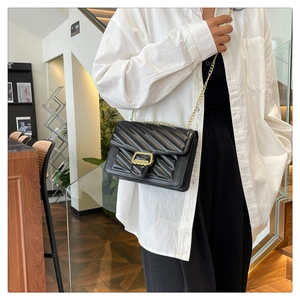 Detail of black quilted crossbody bag with golden chain strap and metallic clasp