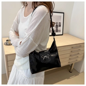 Détail d'un sac seau en PU noir brillant avec un nœud décoratif en métal argenté élégant