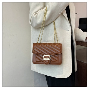 Detail of caramel quilted synthetic leather shoulder bag with golden chain on white blazer