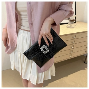 Close-up of black crocodile-embossed leather clutch featuring a sparkling crystal buckle