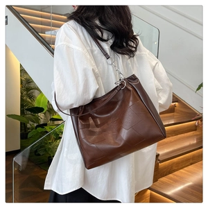 Deep brown oversized leather tote bag shown on shoulder in a minimalist indoor setting