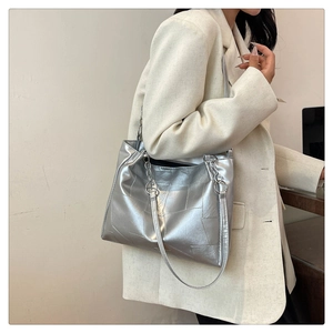 Detail of silver geometric patchwork tote bag with metal chain strap worn on shoulder