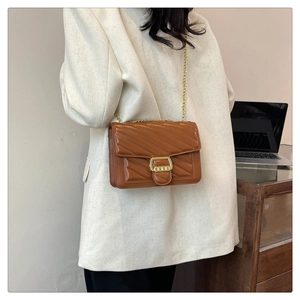 Detail of brown quilted leather bag with V-shaped stitching and golden chain strap