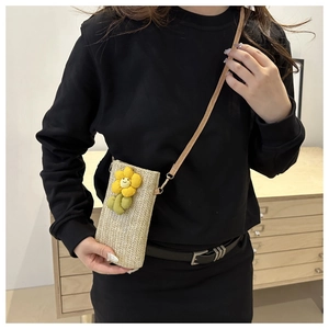 Detailed close-up of handmade woven straw phone bag featuring a yellow flower decorative motif