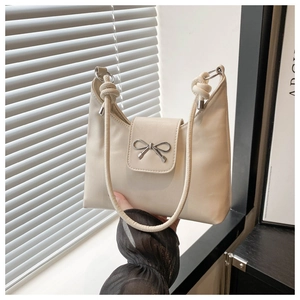 Detail of cream white leather handbag with silver metal bow and knotted shoulder strap