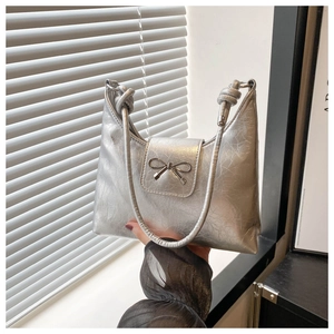 Close-up of silver metallic underarm bag featuring a textured finish and metal bow detail