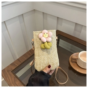 Detail of hand-woven straw phone bag with a pink plush flower charm and leather strap