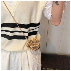 Detail of a gold metallic lip-shaped mini crossbody bag with a fine chain strap on a model