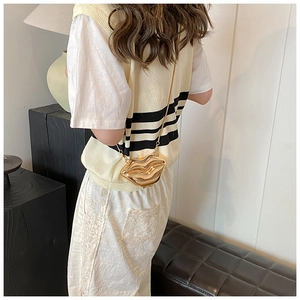 Détail du sac à main doré en forme de lèvres avec fine bandoulière chaîne sur modèle