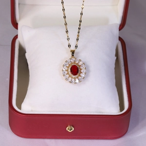 Détail d'un collier en titane doré avec pendentif rubis rouge sur coussin de velours blanc