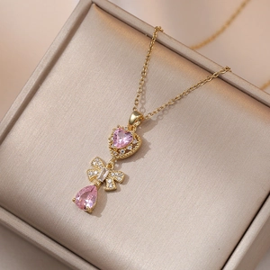 Detail of gold necklace featuring pink heart stone, micro-pave bow and pear drop pendant