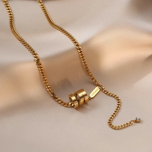 Long collier doré avec pendentif cylindrique évidé sur fond luxueux en satin champagne