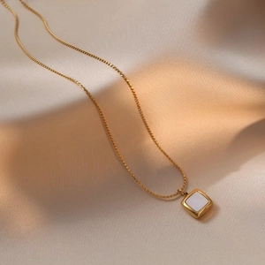 Elegant gold titanium necklace with a square white shell pendant on champagne silk fabric