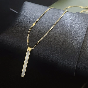 Detail of a slender gold titanium bar necklace with a white mother of pearl inlay