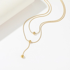 Double-layered gold snake chain necklace with three beads on a minimalist background