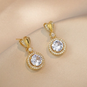 Elegant gold heart earrings with sparkling zircon drop on champagne silk fabric background