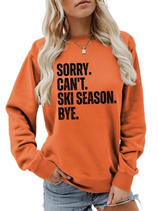 Detail of orange crewneck sweatshirt with 'SORRY CAN'T SKI SEASON' black bold typography