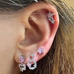 Close-up of pink zircon ear studs and heart pendants worn on the ear helix and lobe