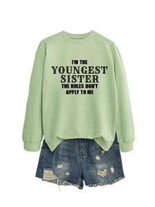 Detail of sage green sweatshirt with black slogan print paired with ripped denim shorts