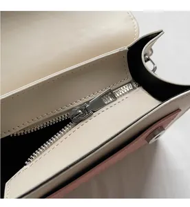 Close-up of smooth silver zipper on off-white leather bag with pink piping details