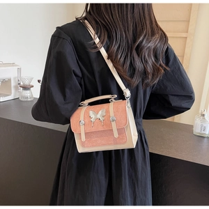 Detail of pink frosted crossbody bag with silver butterfly charm on a model in a cafe