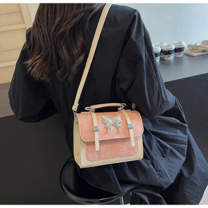 Detail of a pink and white crossbody bag with a silver butterfly clasp on a female model