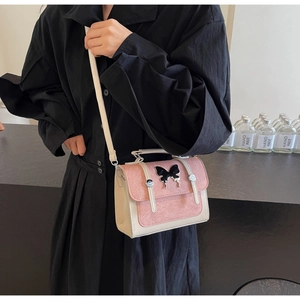 Detail of pink and white crossbody bag with a distinctive black butterfly clasp ornament