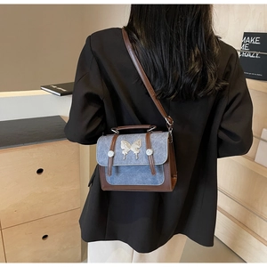 Detail of blue denim and brown leather crossbody bag with silver butterfly buckle